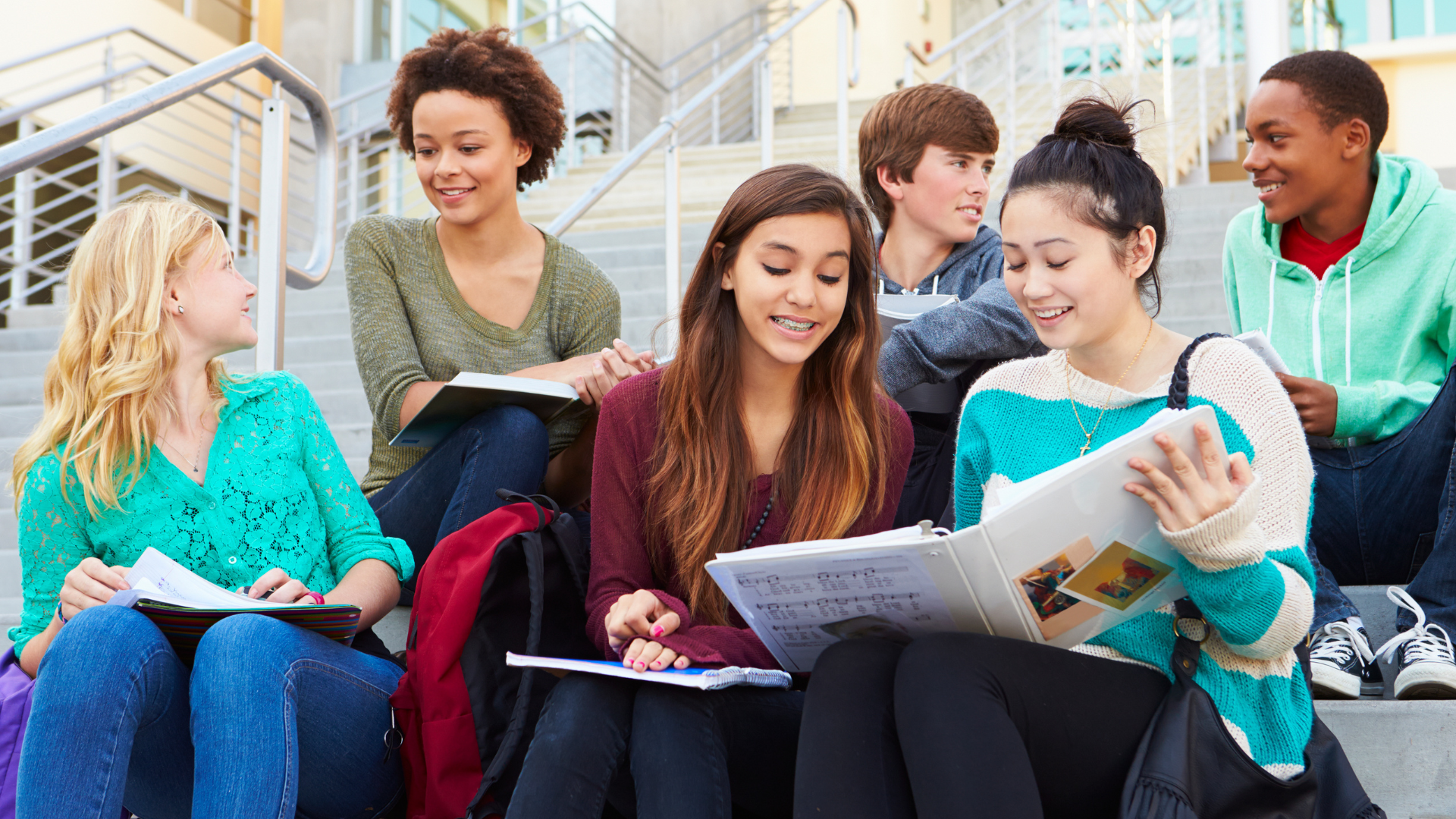 students sitting and chatting on the steps of a modern high school building