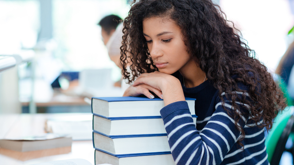 a female college students resting her head on a stack of books