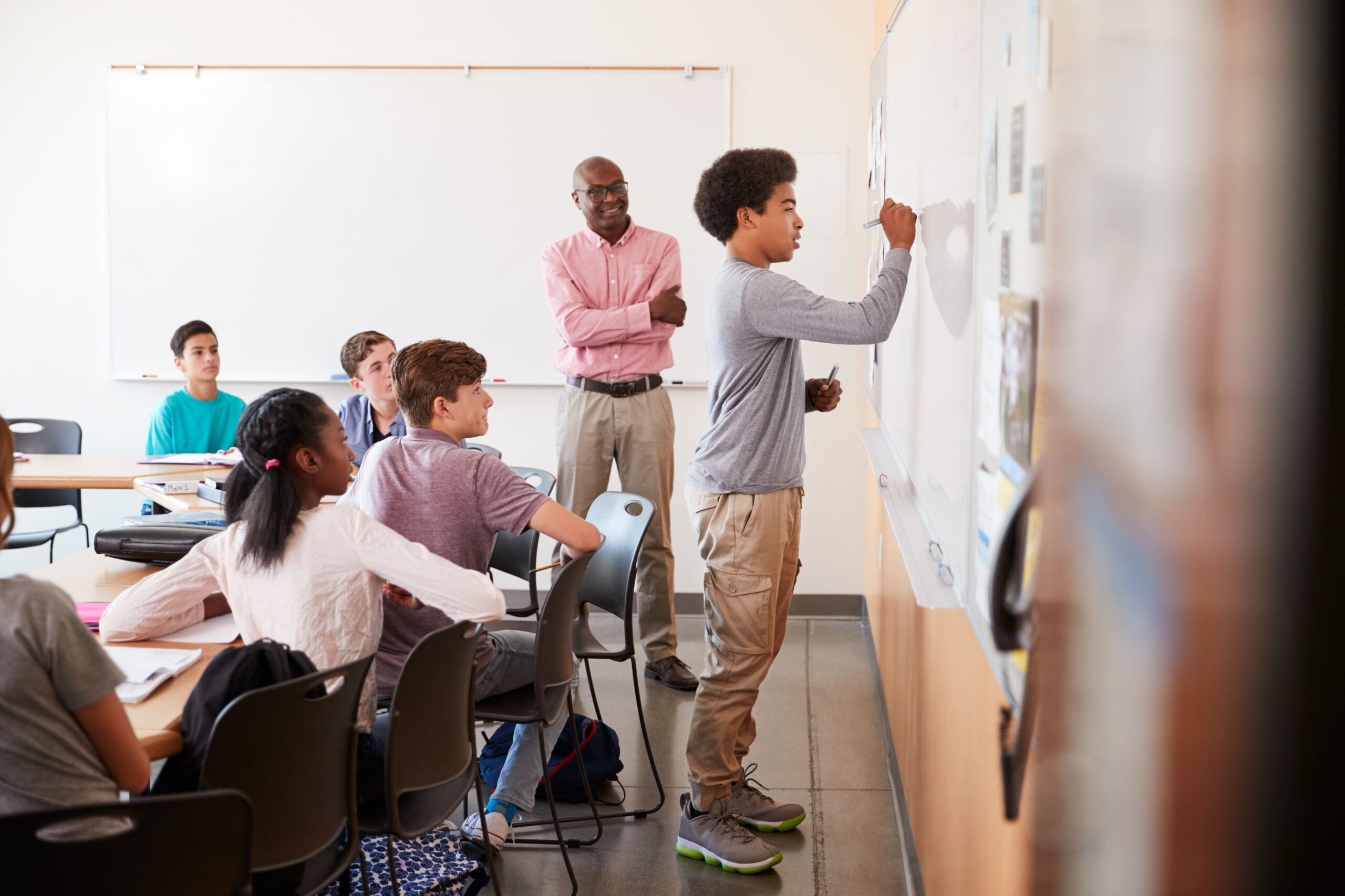 student at a whiteboard with his classmates and teacher behind him