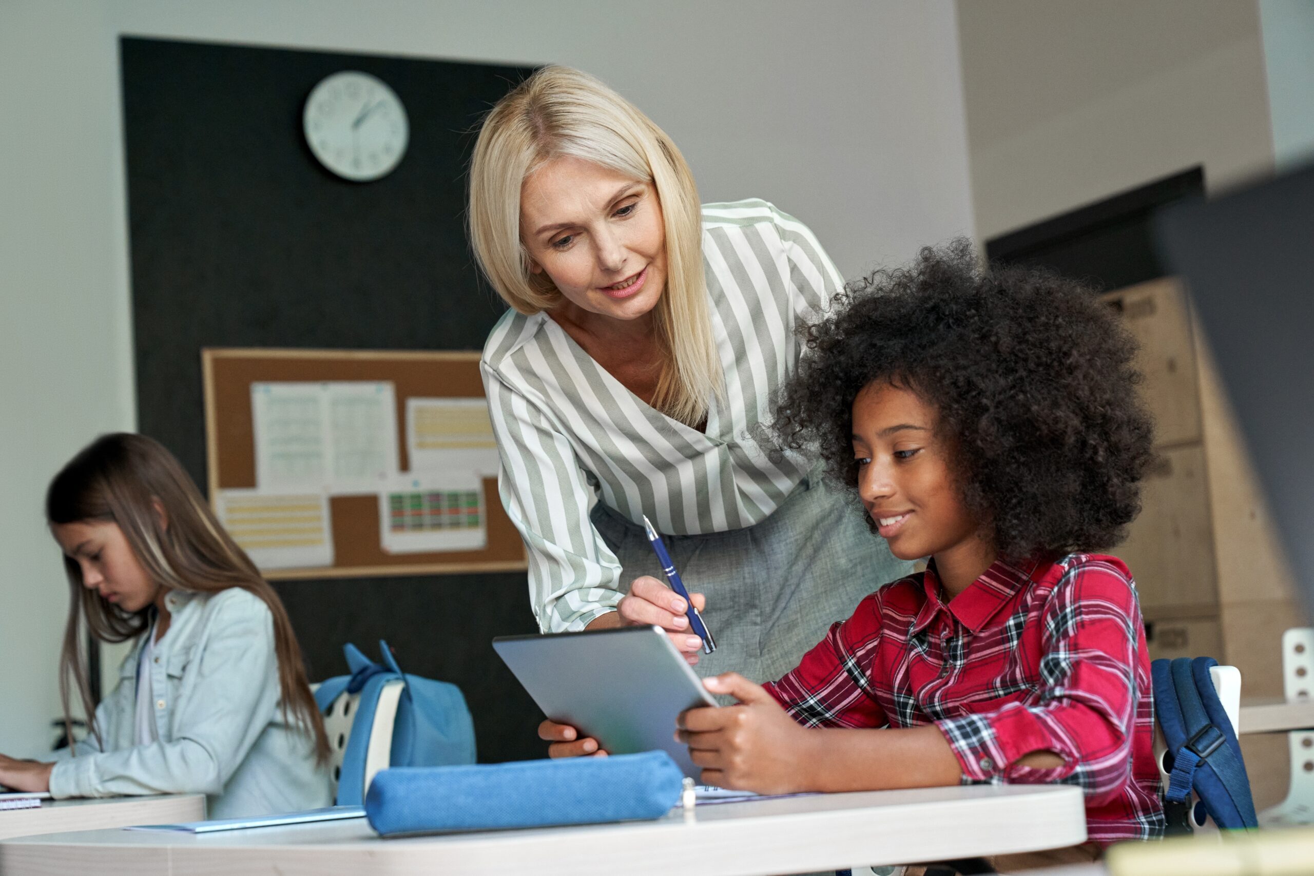 a teacher leaning in to instruct a student at their desk