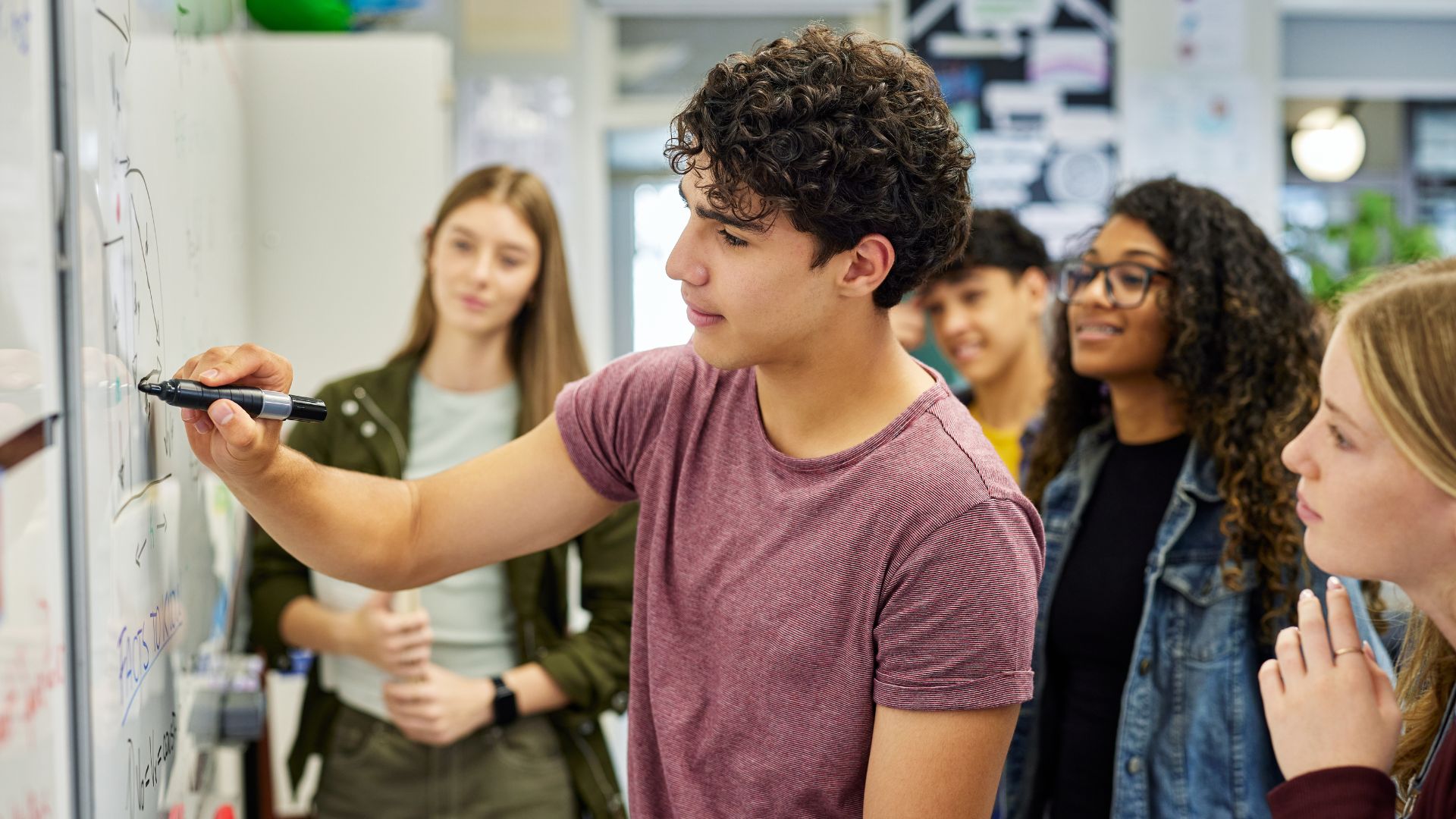 a teenage student writing math equations on a white board while three other students look on