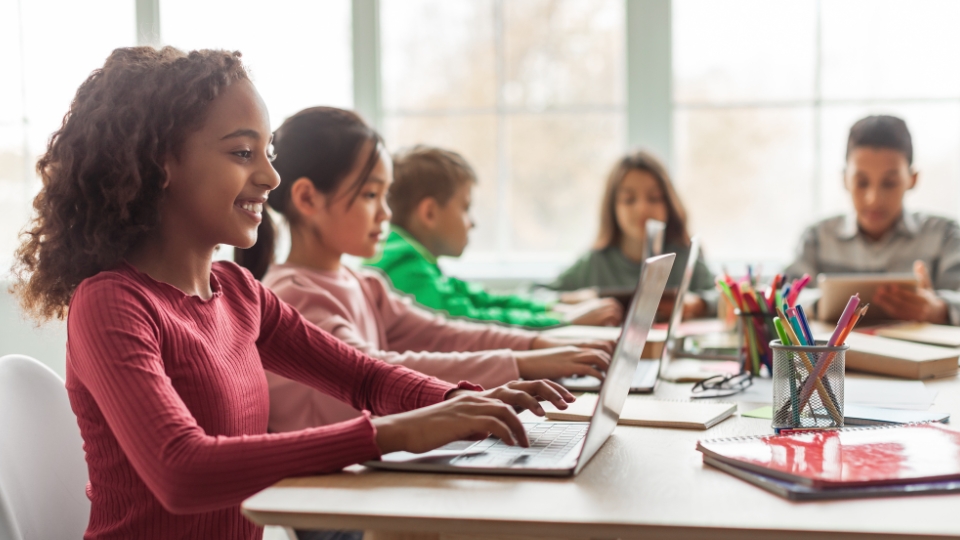 young elementary students at a desk, each with laptops